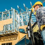 Home contractor with a hard hat stepping out of a vehicle looking up a construction site.