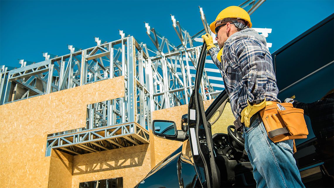 Home contractor with a hard hat stepping out of a vehicle looking up a construction site.