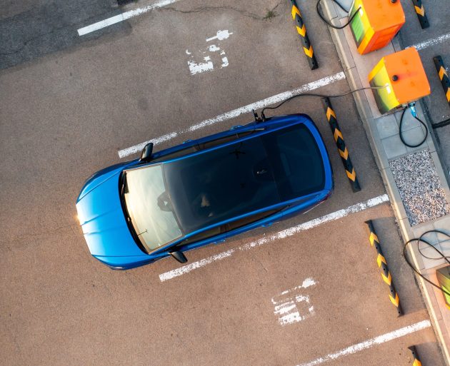 Aerial view of blue electric fleet vehicle charging in a parking lot