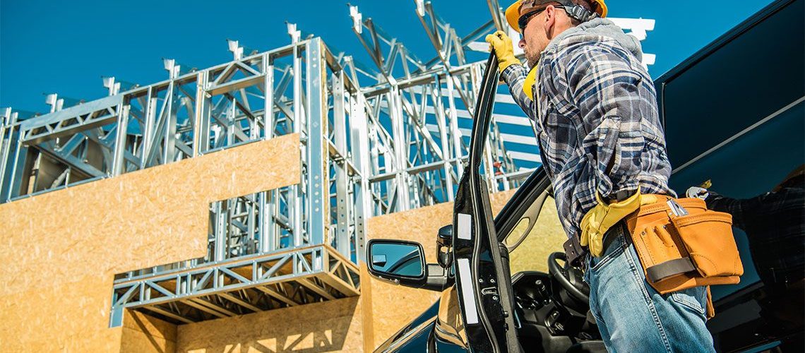 Home contractor with a hard hat stepping out of a vehicle looking up a construction site.